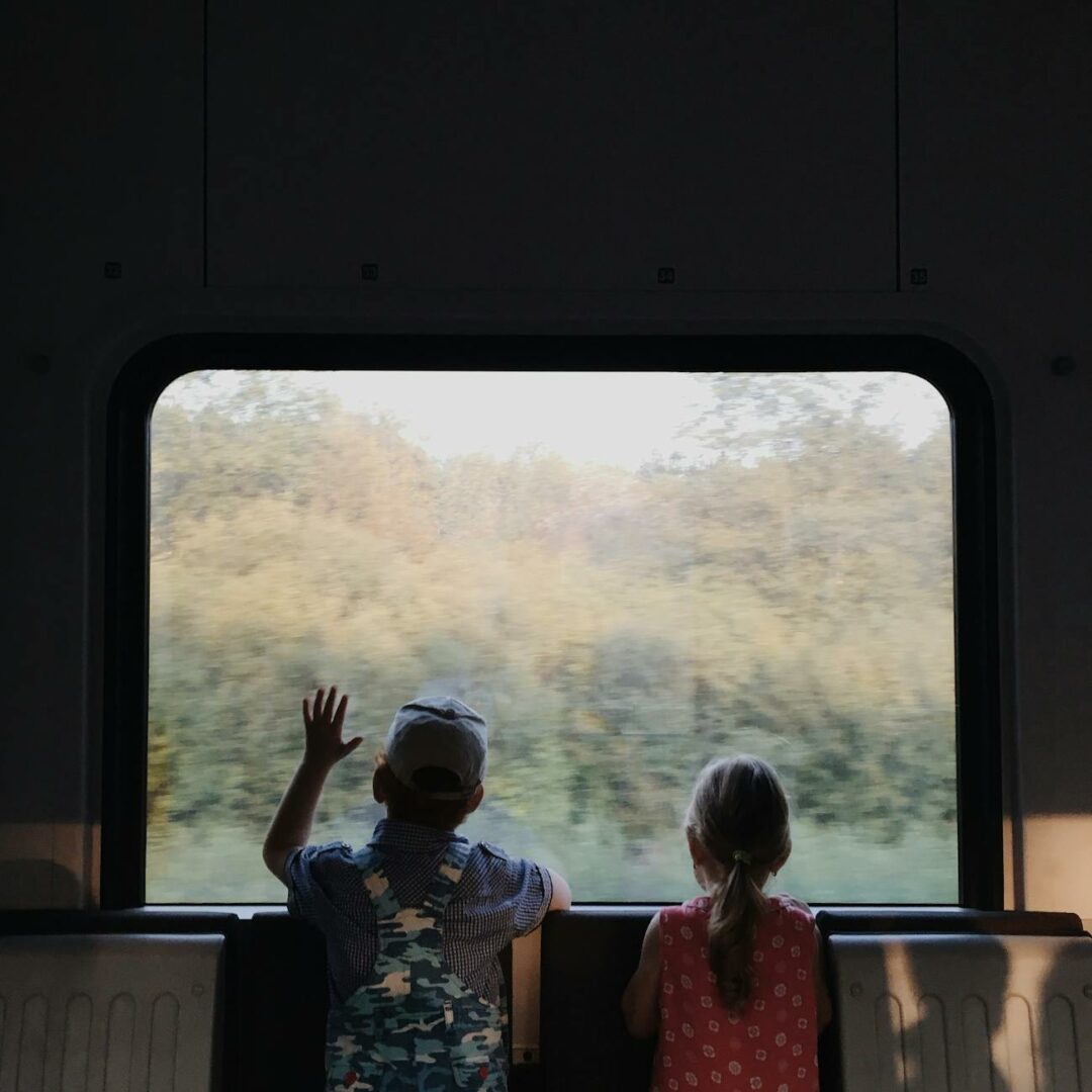 a boy and a girl looking outside the window of a train