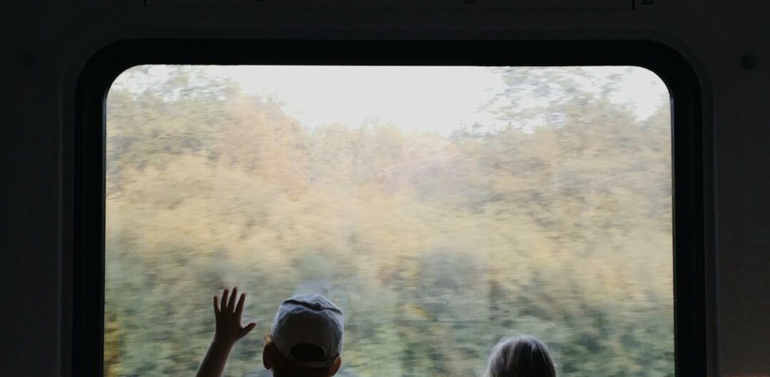 a boy and a girl looking outside the window of a train